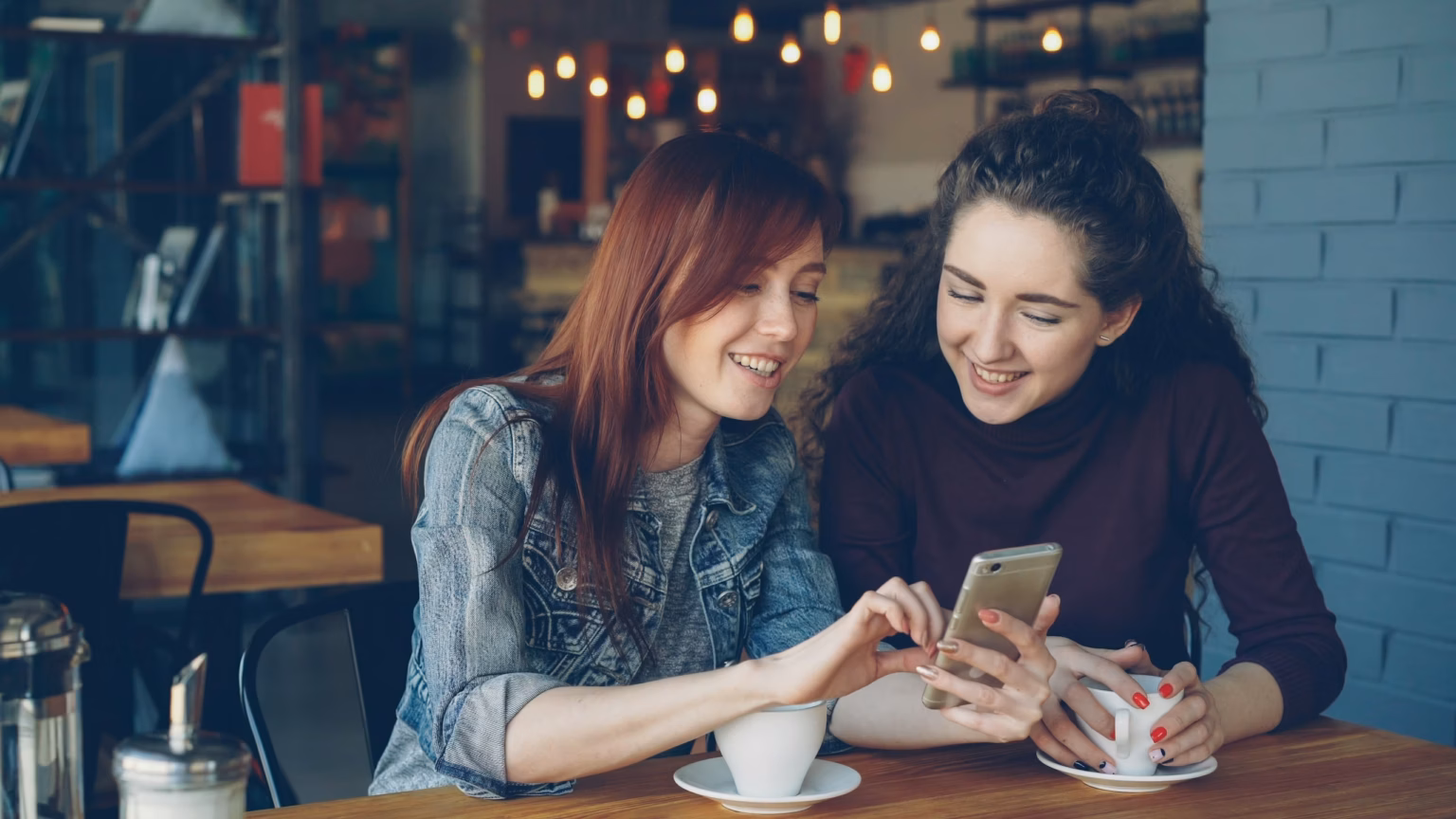 Two friends smile while looking at a phone.