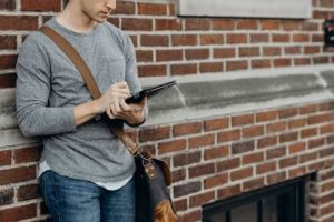 standing man in gray crew-neck long-sleeved shirt leaning on brown bricked wall
